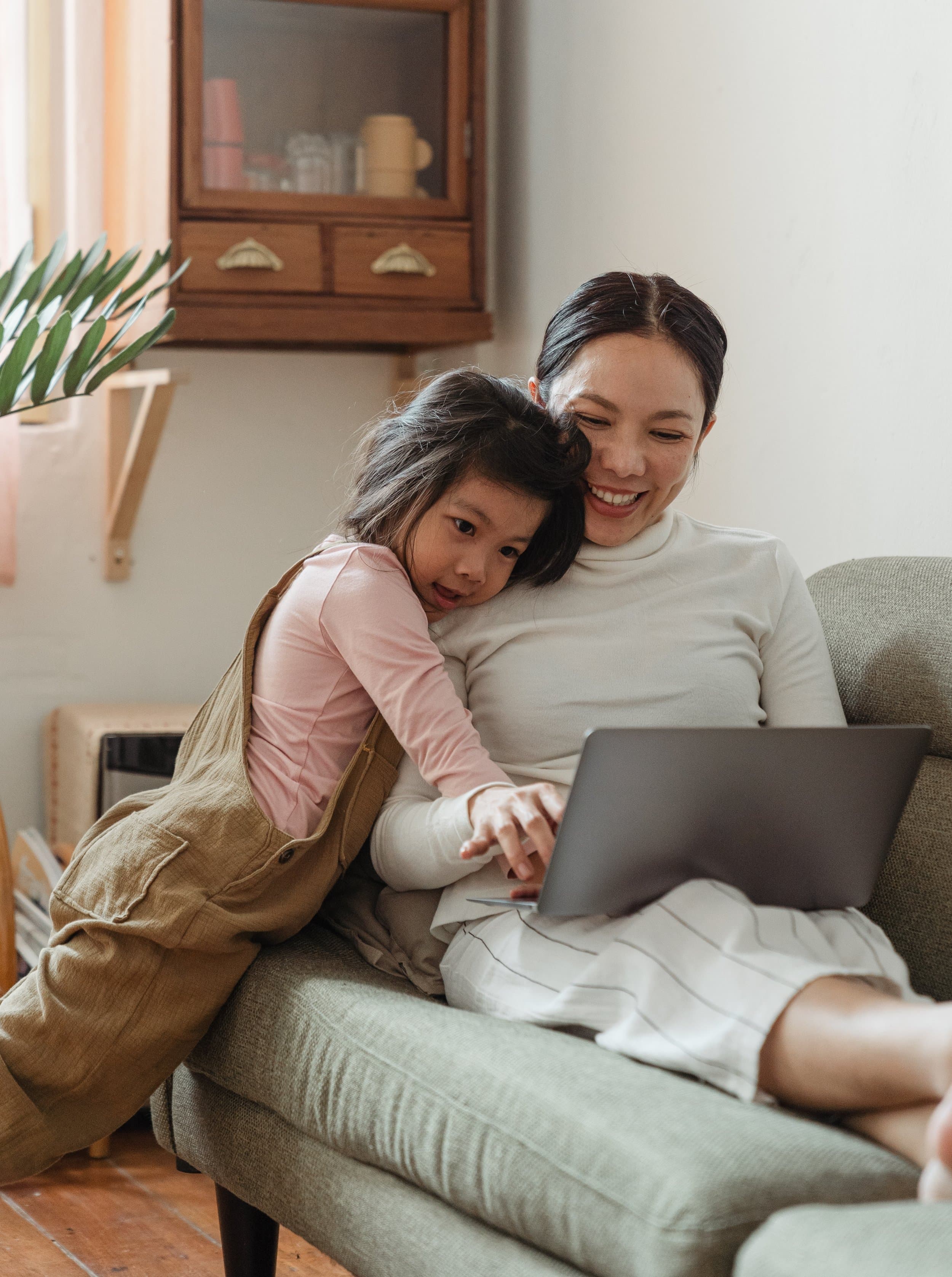 Parent and child sitting together on a couch using a laptop during a virtual speech therapy or learning activity at home.