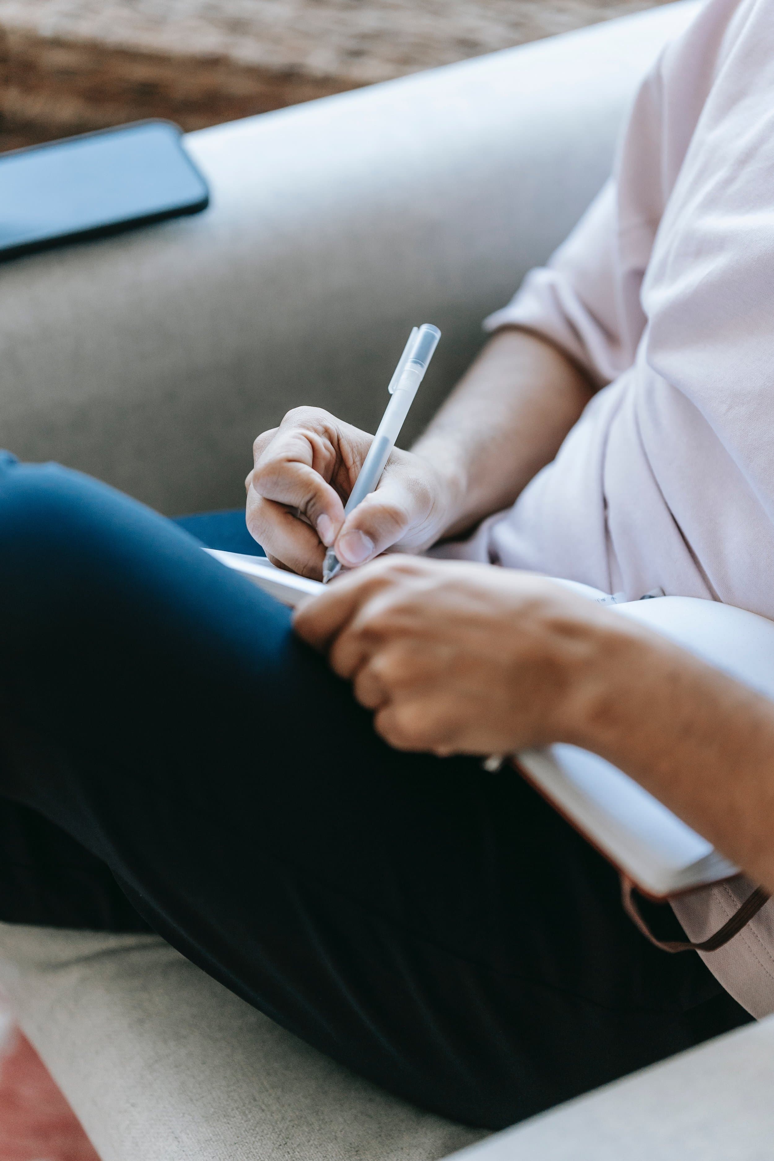 A parent sitting on a couch, writing in a notebook.
